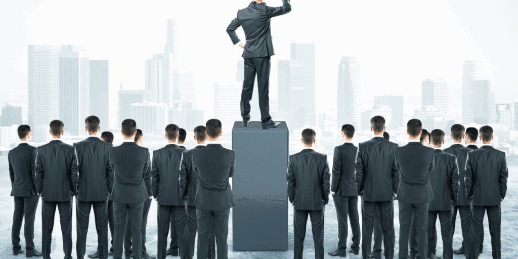 A businessman stands elevated on a pedestal above others in suits.