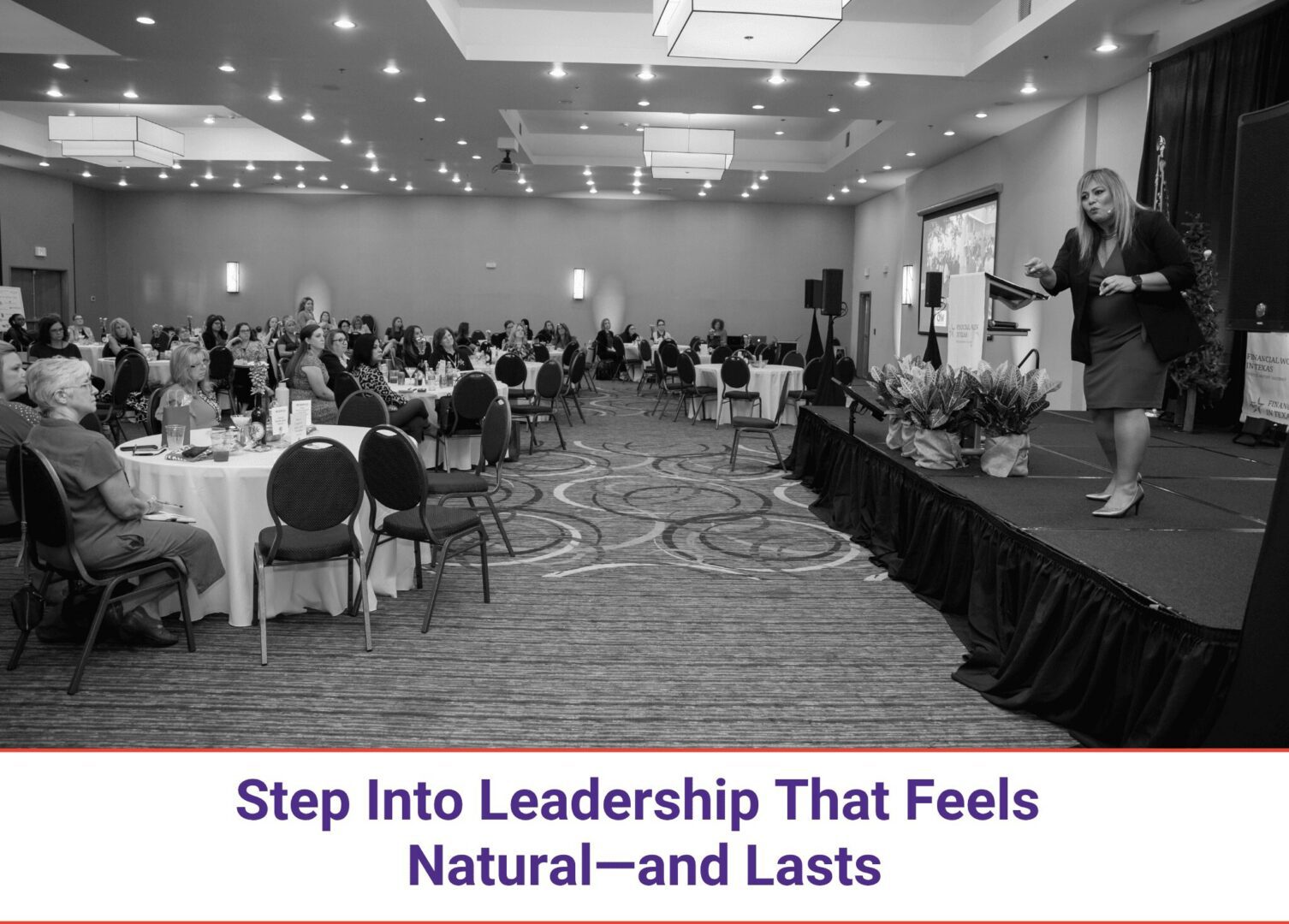 A conference room with attendees and a speaker on stage.